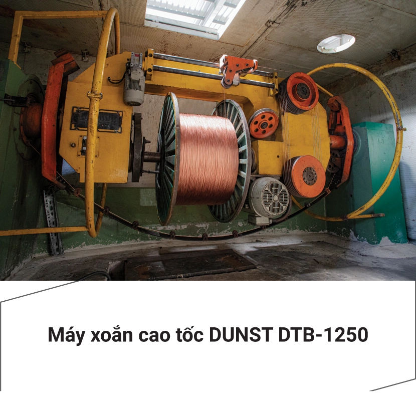 Máy xoắn cao tốc DUNST DTB 1250 với cuộn dây đồng lớn, trục quay và bánh đai màu cam, được đặt trong lồng bảo vệ có trần cao và ánh sáng tự nhiên từ cửa sổ.