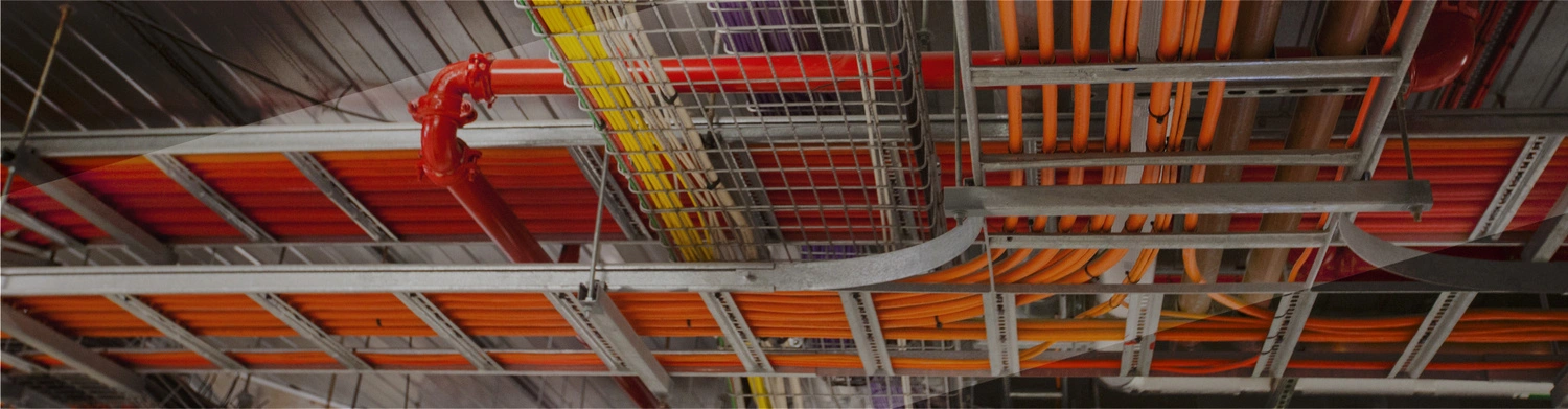 Residential electrical wiring arranged on a metal frame at a construction site, integrated with plumbing pipes and steel ceilings, serving electrical systems for homes, apartments, and commercial buildings.
